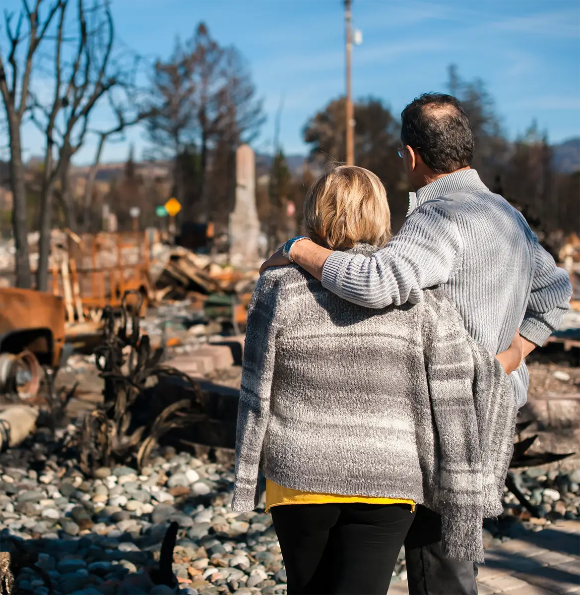 A man and wife hugging while observing their burnt-down Los Angeles home.